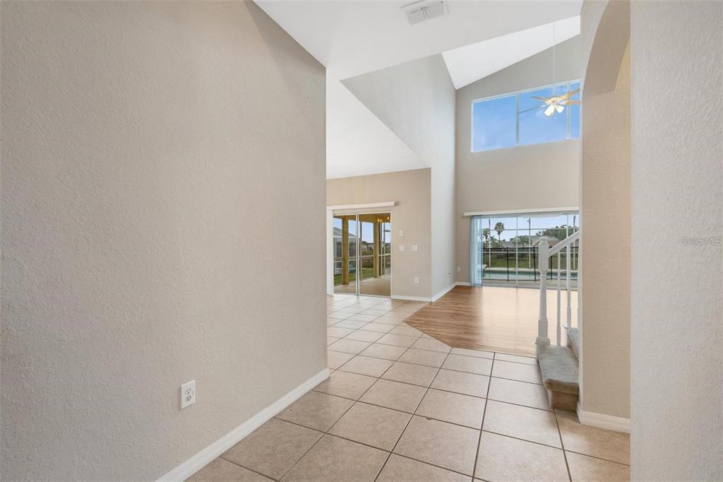 A tiled entryway leads to a living area with high ceilings, wood flooring, and pool views — 318 WINDSOR PLACE, DAVENPORT, FL
