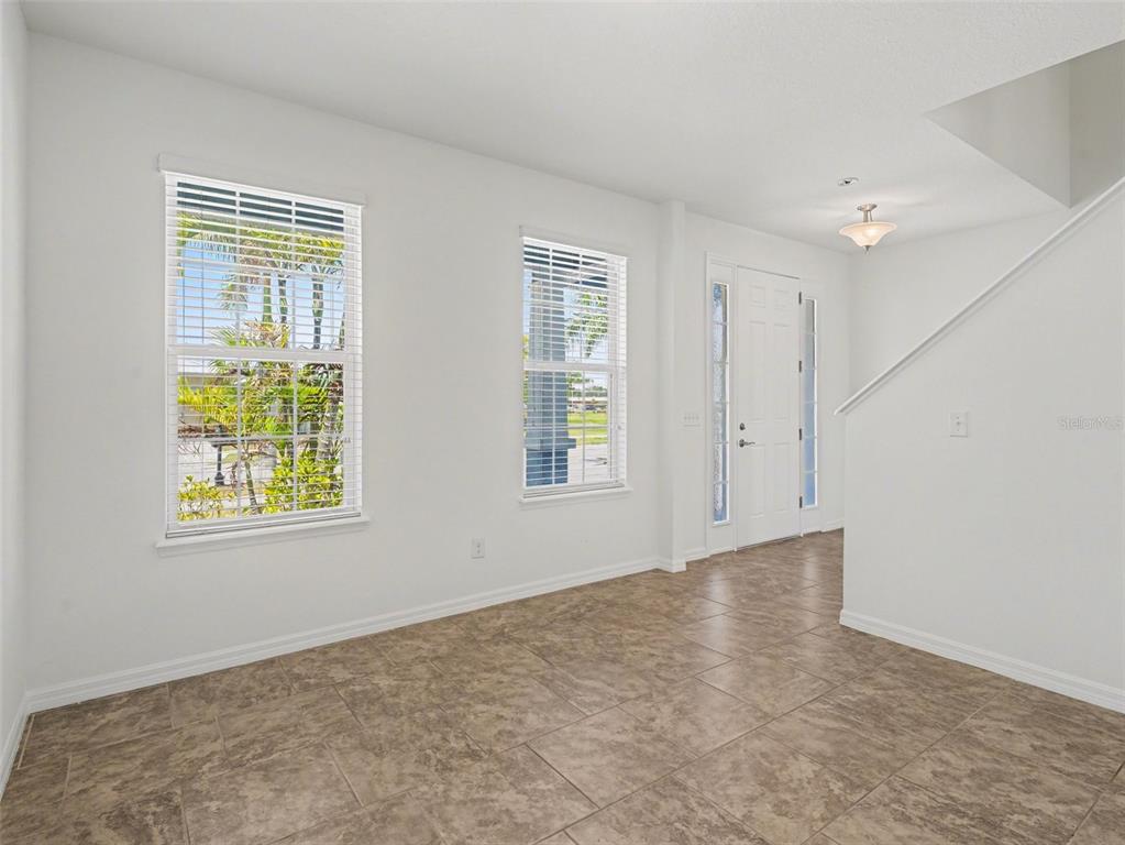 An empty room features white walls, tile flooring, two windows, and a front entryway — 6417 KEY ISLAND AVE, APOLLO BEACH, FL