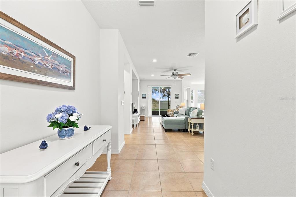 A white console table sits in a tiled hallway leading to a living room with furniture — 381 SILVER MAPLE ROAD, GROVELAND, FL