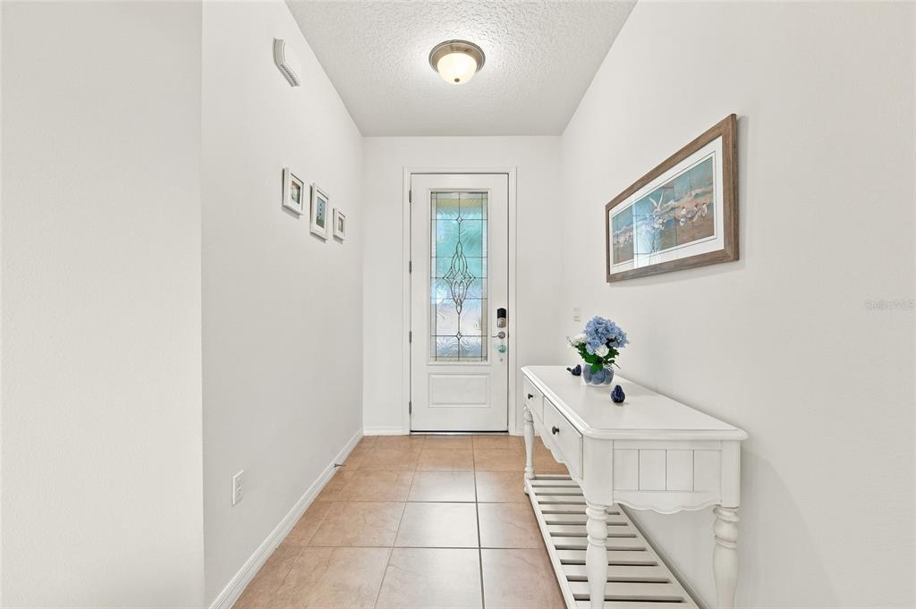 A bright entryway features tiled flooring, a white console table, and a glass-paneled front door — 381 SILVER MAPLE ROAD, GROVELAND, FL