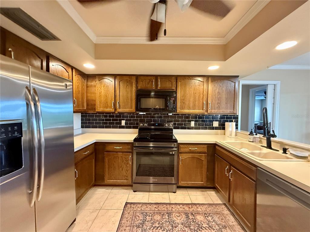 A kitchen features wood cabinets, stainless steel appliances, a black subway tile backsplash, and tile flooring — 1739 LAKE MARION DRIVE, APOPKA, FL