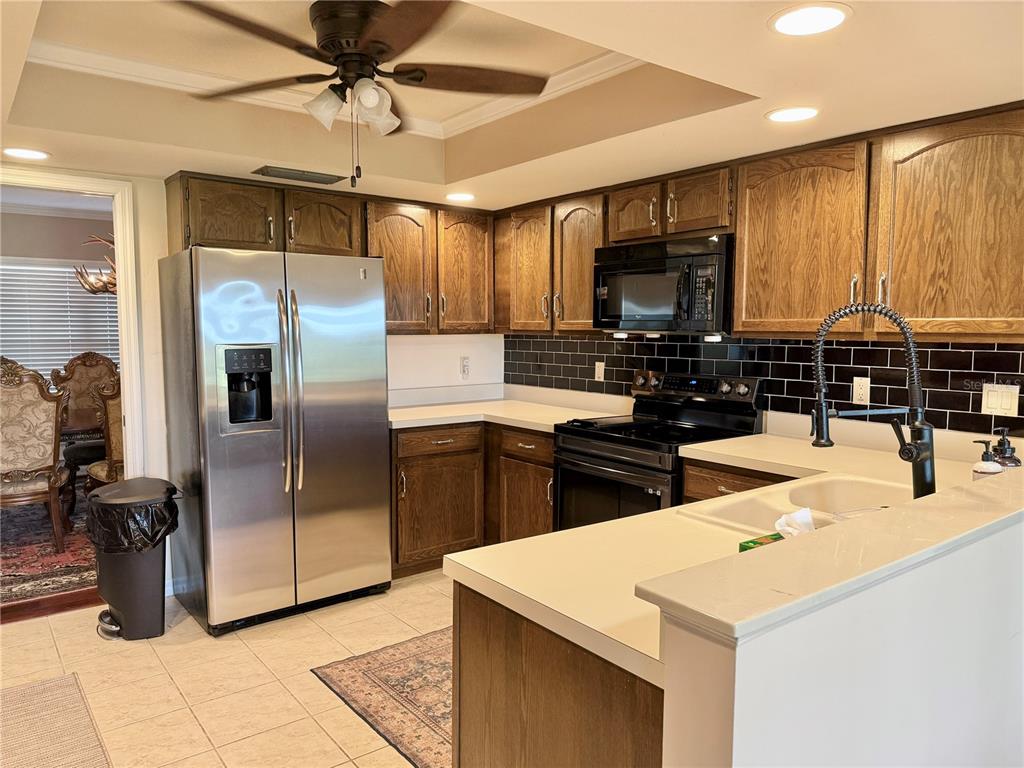 A kitchen features wood cabinets, stainless steel appliances, white countertops, and a black subway tile backsplash — 1739 LAKE MARION DRIVE, APOPKA, FL