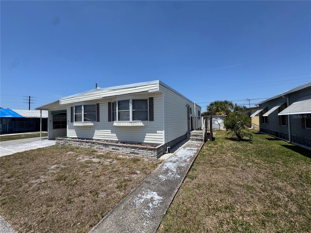 A single-story manufactured home with light siding, a concrete walkway, and a brick planter box — 1111 49TH AVE TERRACE W, BRADENTON, FL