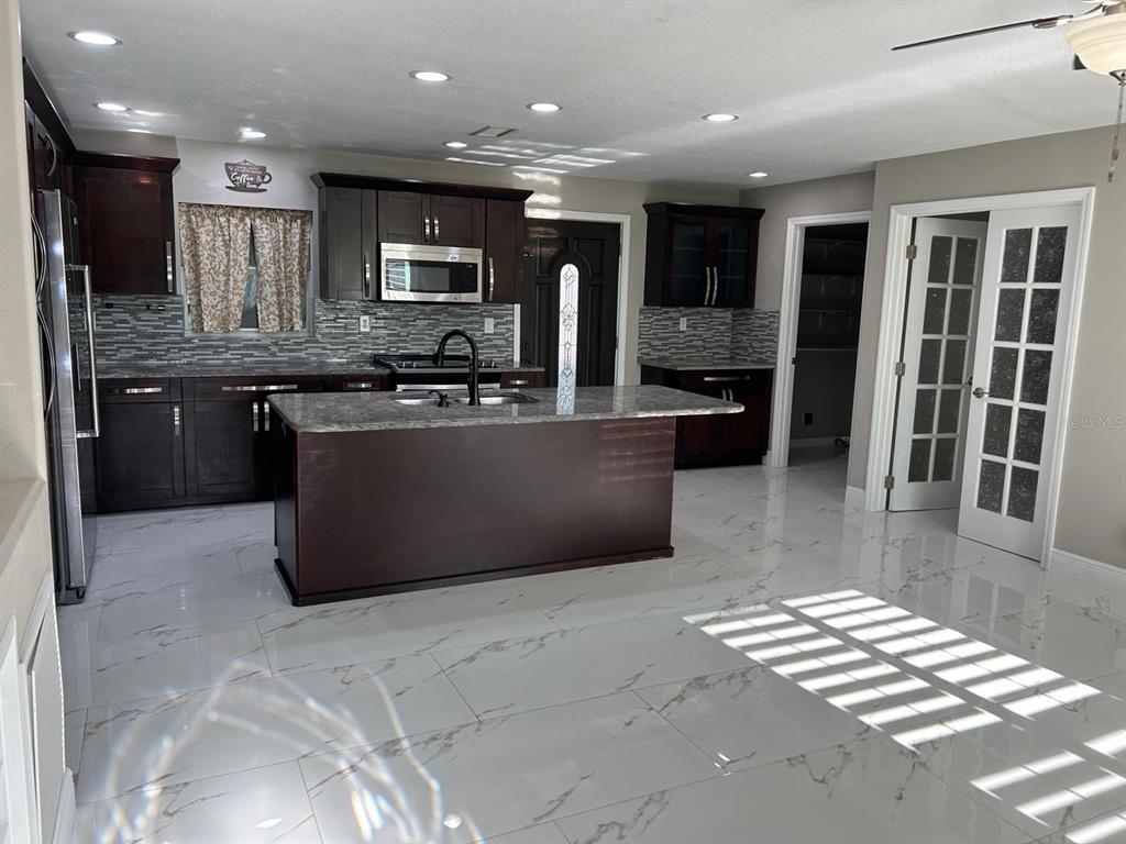 A kitchen with a granite island and stainless steel dishwasher overlooks a room with tile floors — 9724 TOM FOLSOM ROAD, THONOTOSASSA, FL
