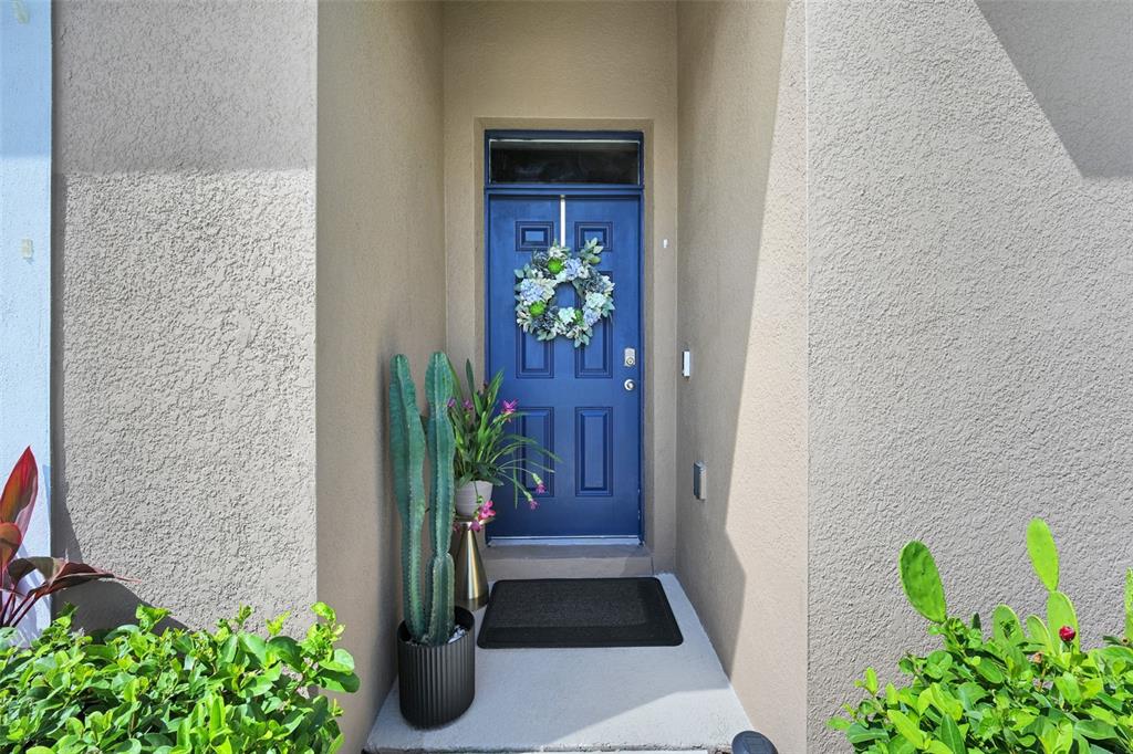 A blue front door with a wreath sits in a recessed entryway with potted plants — 5457 HAYLOFT DRIVE, APOPKA, FL