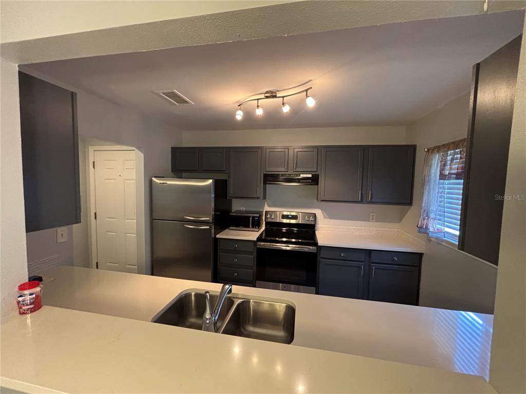 A galley kitchen features dark cabinets, stainless steel appliances, white countertops, and tiled flooring — 1968 TOUCAN WAY UNIT 1404, SARASOTA, FL
