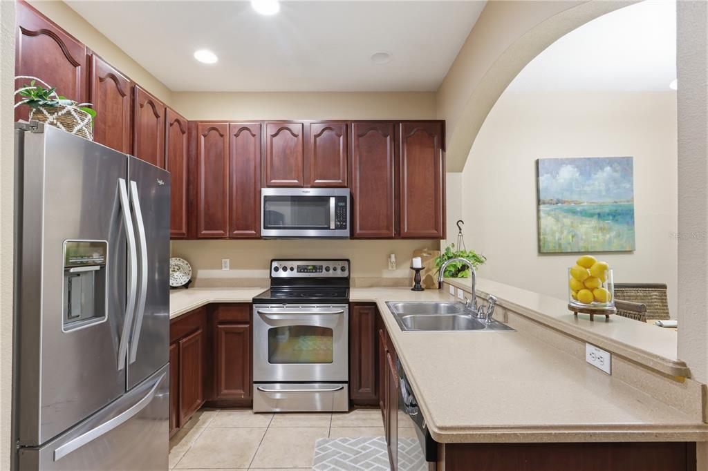 A kitchen with dark wood cabinets, stainless steel appliances, and beige countertops — 10291 PARK COMMONS DRIVE, ORLANDO, FL