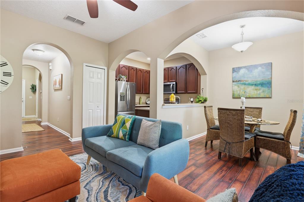 A living room with wood-look flooring leads to an arched opening into the kitchen — 10291 PARK COMMONS DRIVE, ORLANDO, FL
