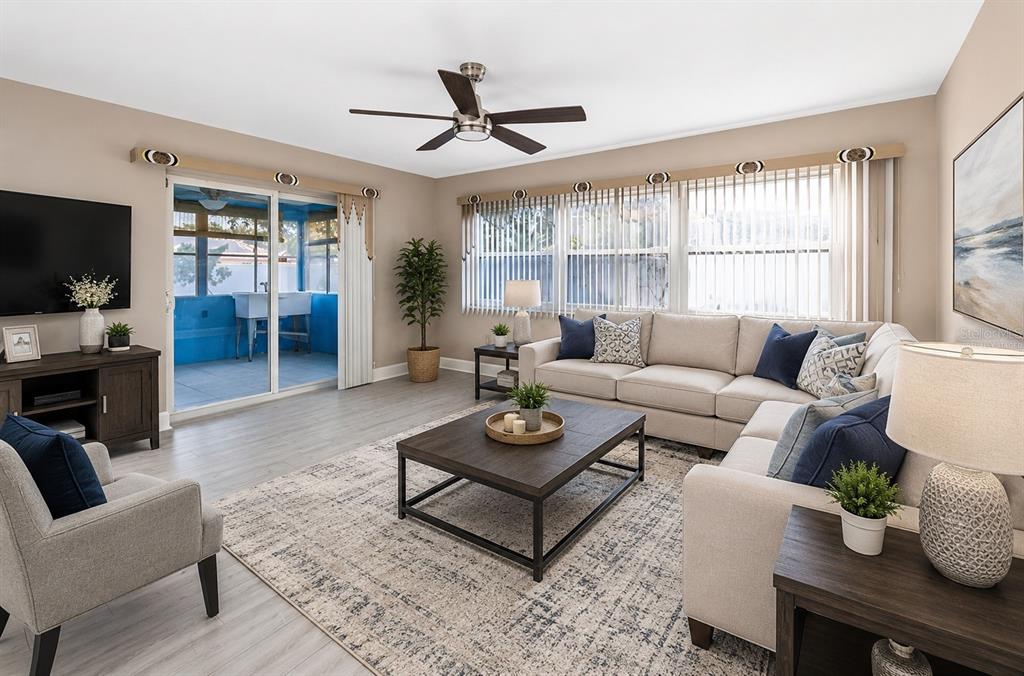 A spacious living area features light wood-look flooring, beige walls, and an adjacent kitchen — 1929 VALENCIA WAY, CLEARWATER, FL