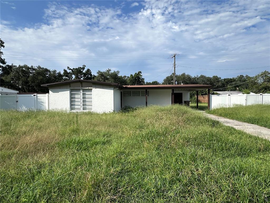 A single-story white brick house with a carport sits behind an overgrown grassy lawn — 503 BROXBURN AVENUE, TEMPLE TERRACE, FL