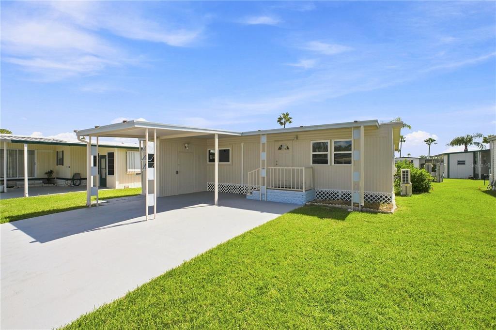A single-story manufactured home with a carport, light siding, and a small front porch — 10912 JUSTICE DRIVE, PORT RICHEY, FL