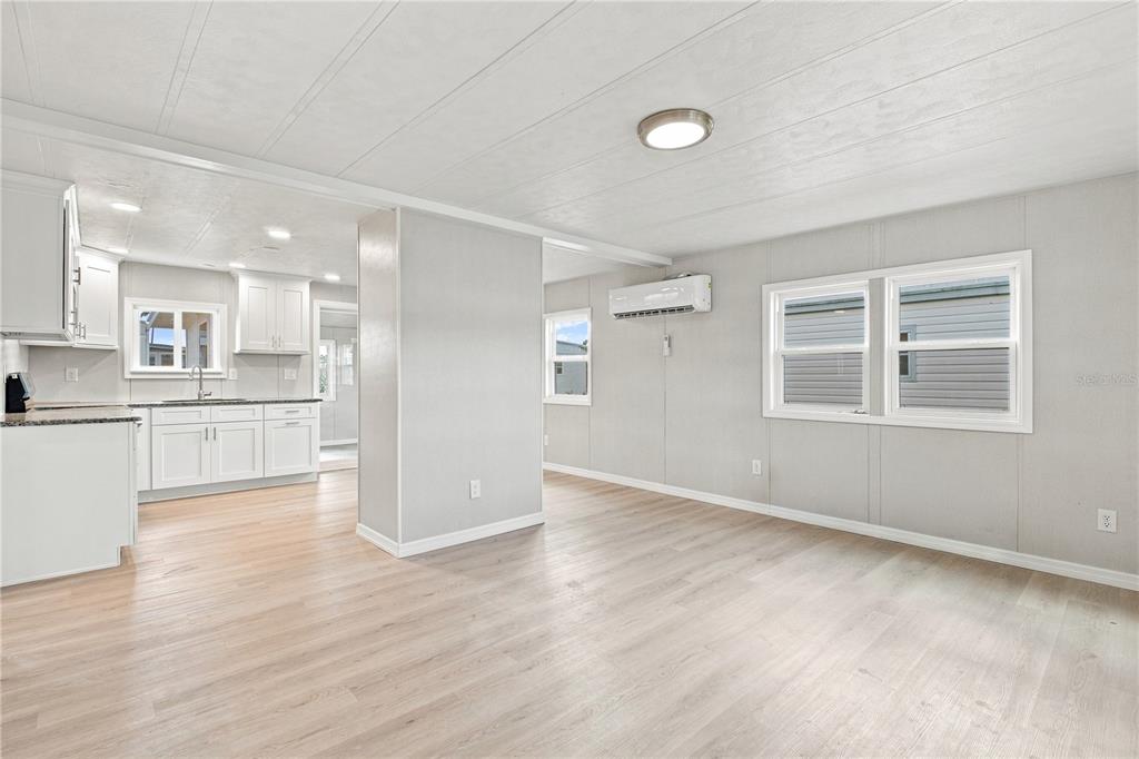 A bright living room with light wood flooring, white walls, and an open kitchen view — 10912 JUSTICE DRIVE, PORT RICHEY, FL