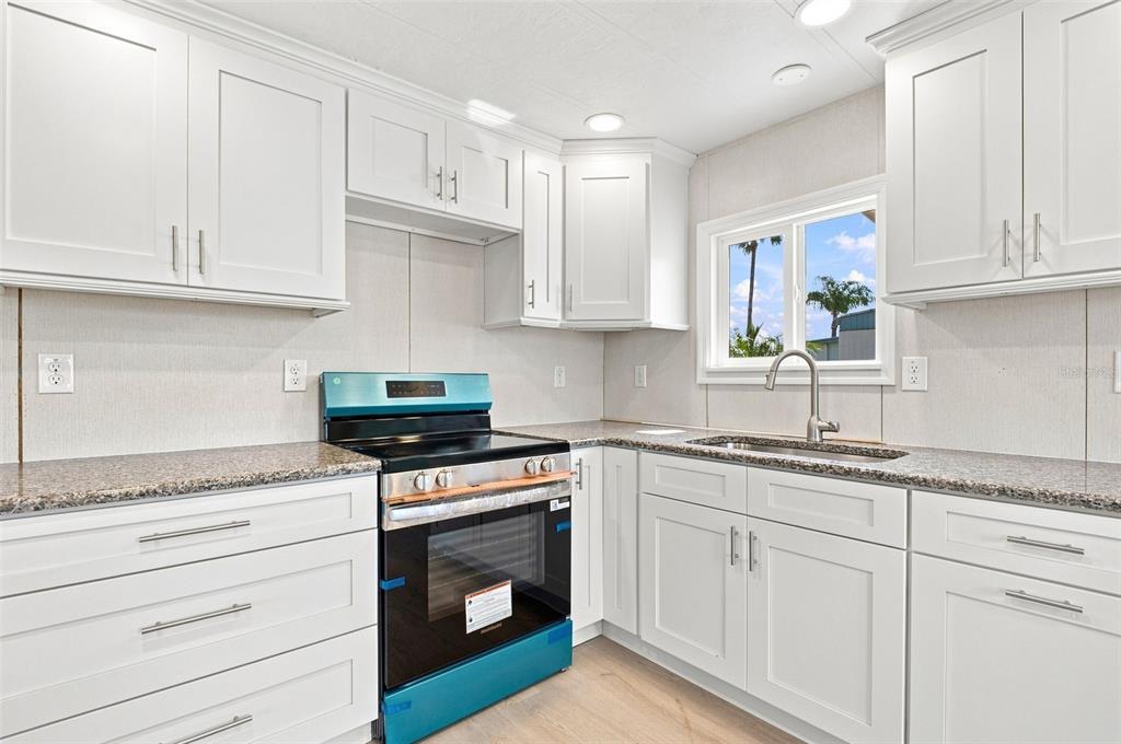 A kitchen features white cabinets, granite countertops, a stainless steel sink, and a new stove — 10912 JUSTICE DRIVE, PORT RICHEY, FL