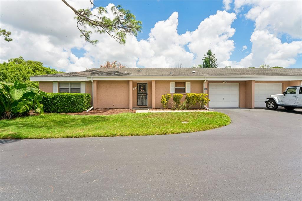 A single-story house exterior features a white garage door, tan stucco walls, and a driveway — 1520 PALMER COURT, PALM HARBOR, FL