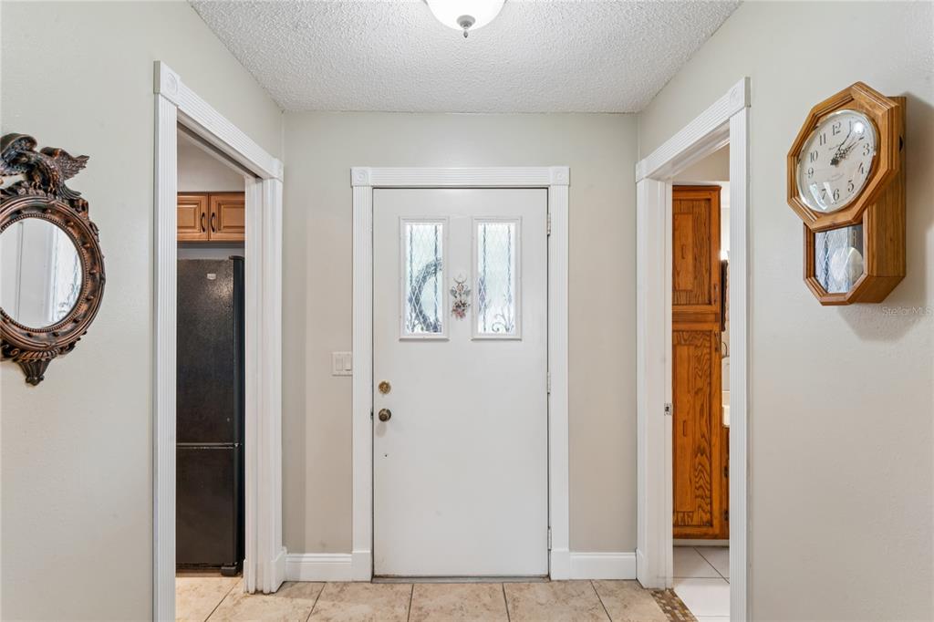 A tiled entryway features a white front door flanked by two doorways and a wall clock — 1520 PALMER COURT, PALM HARBOR, FL