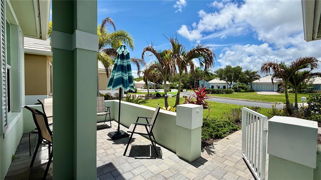 A paved patio with outdoor furniture and a striped umbrella overlooks a landscaped residential street — 1330 SAINT CATHERINES CIRCLE, VERO BEACH, FL