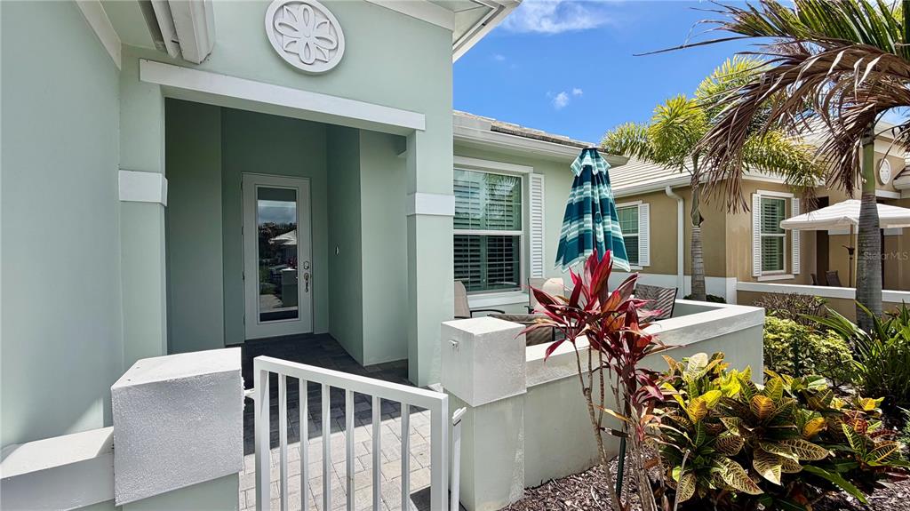 A light green house exterior features a front patio, white gate, and tropical landscaping — 1330 SAINT CATHERINES CIRCLE, VERO BEACH, FL