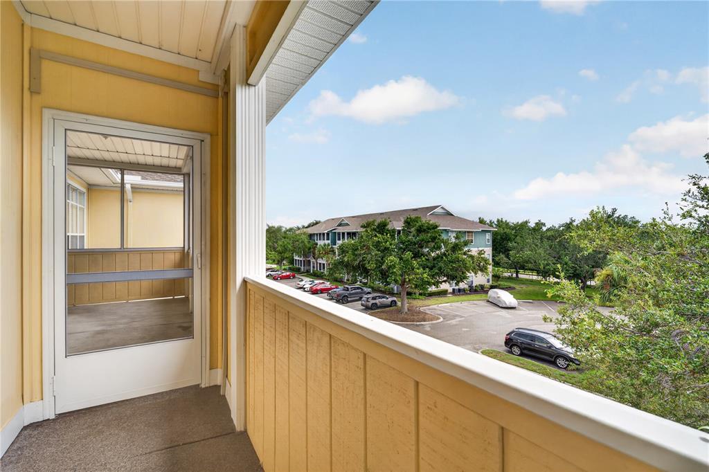 A covered balcony with yellow siding overlooks a parking lot and a neighboring apartment building — 4802 51ST STREET W UNIT 1912, BRADENTON, FL