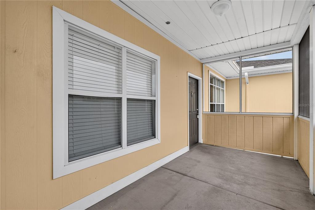 A covered patio features a concrete floor, beige siding, a window with blinds, and a door — 4802 51ST STREET W UNIT 1912, BRADENTON, FL