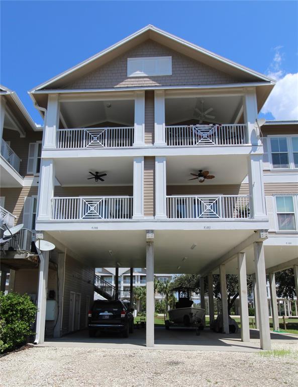 A three-story elevated residential building with balconies and a gravel parking area underneath — 221 3RD AVENUE E UNIT F-102, HORSESHOE BEACH, FL