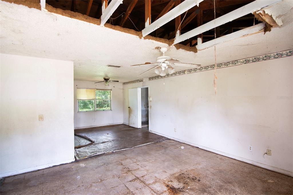 A dilapidated living room features a large ceiling hole exposing the wooden roof rafters — 504 N 18TH STREET, PALATKA, FL