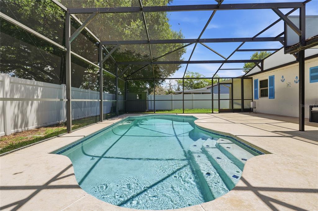 A screened-in swimming pool with concrete decking sits in a backyard enclosed by white fencing — 133 REBECCA DRIVE NE, WINTER HAVEN, FL