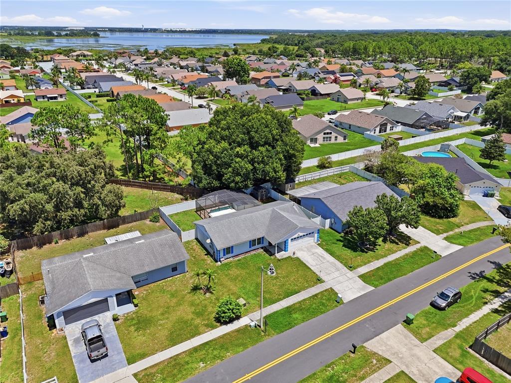 An aerial view shows a suburban neighborhood with houses, lawns, and a nearby lake — 133 REBECCA DRIVE NE, WINTER HAVEN, FL