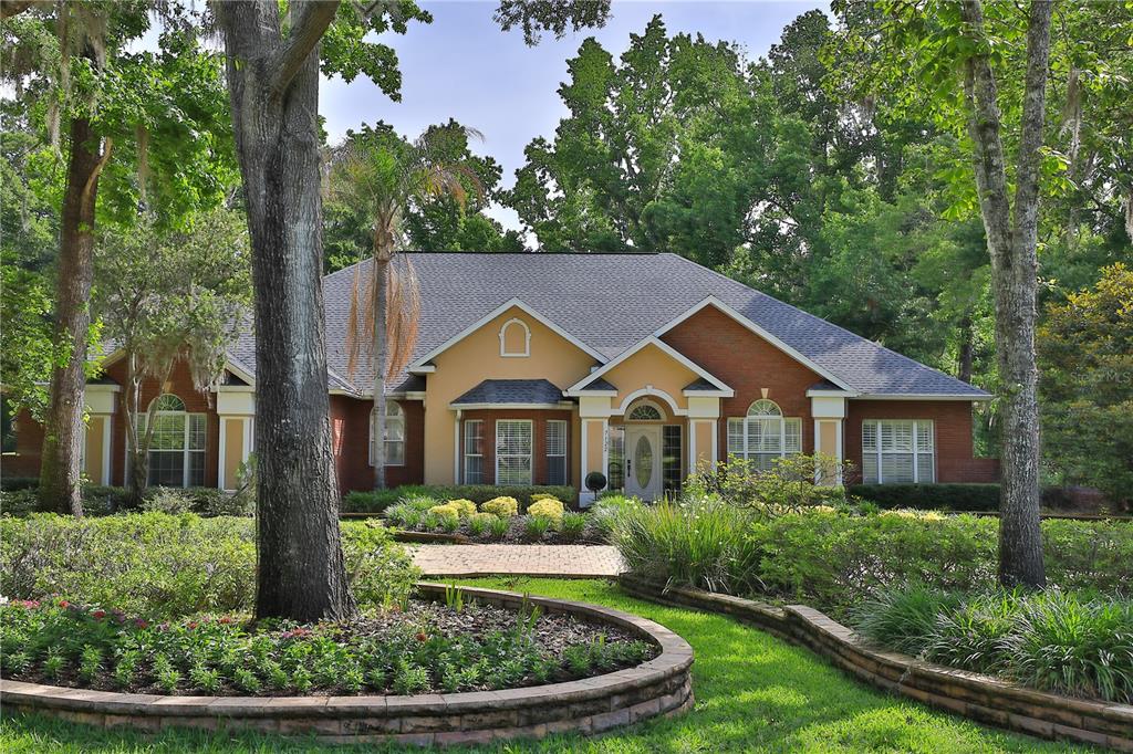 A single-story brick and stucco house with a landscaped front yard and mature trees — 7122 SE 12TH CIRCLE, OCALA, FL