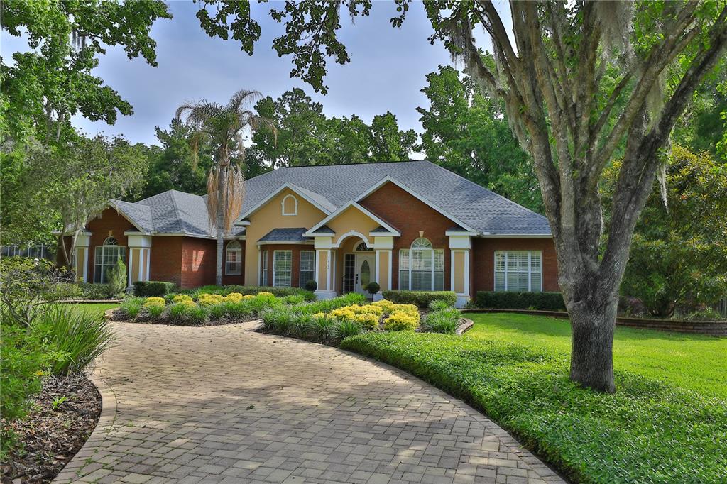 A brick house with a paved driveway and landscaped yard sits among mature trees — 7122 SE 12TH CIRCLE, OCALA, FL