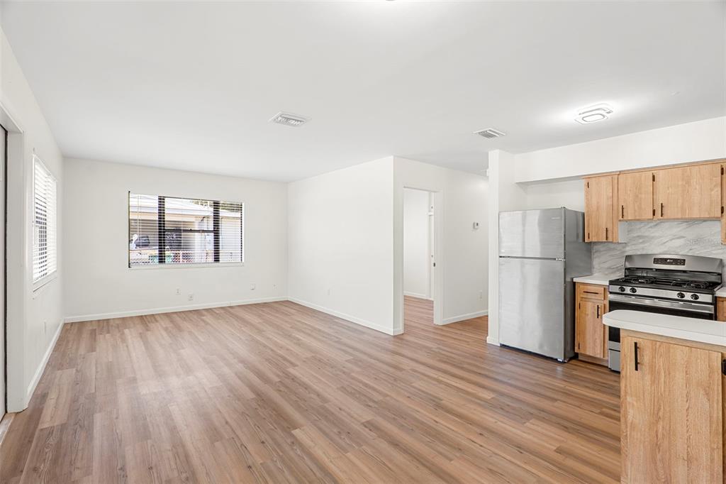 An open-concept room features light wood-look flooring, white walls, and a kitchen with stainless appliances — 2189 S SMATHERS CIRCLE, MELBOURNE, FL