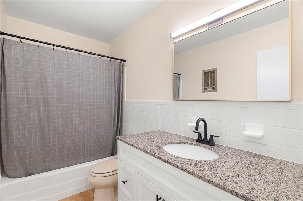 A bathroom features a granite vanity, white cabinets, a shower curtain, and a wall mirror — 2189 S SMATHERS CIRCLE, MELBOURNE, FL