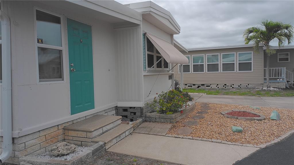 A mobile home exterior features a teal front door, concrete steps, and a gravel yard — 7234 MOUNT FAIRFIELD ROAD NE UNIT 529, ST PETERSBURG, FL