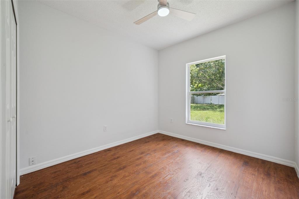 An empty bedroom features light gray walls, wood-look flooring, a ceiling fan, and a window — 20 COVENTRY COURT, KISSIMMEE, FL