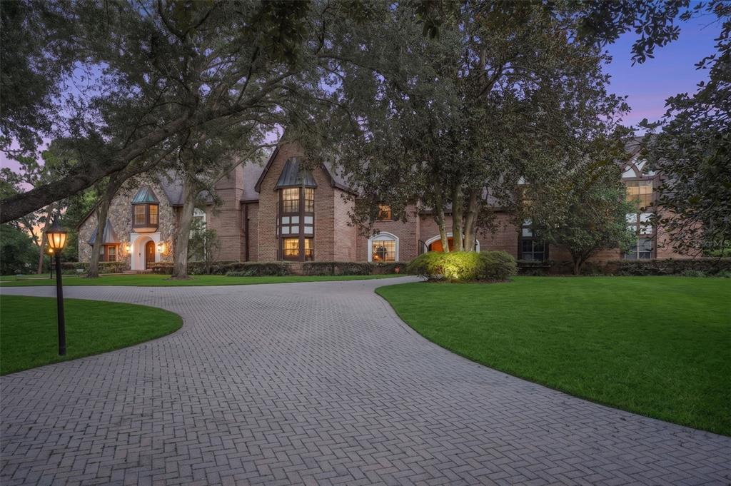 A large brick house with a paved driveway and mature trees at dusk — 810 SWEETWATER CLUB BOULEVARD, LONGWOOD, FL