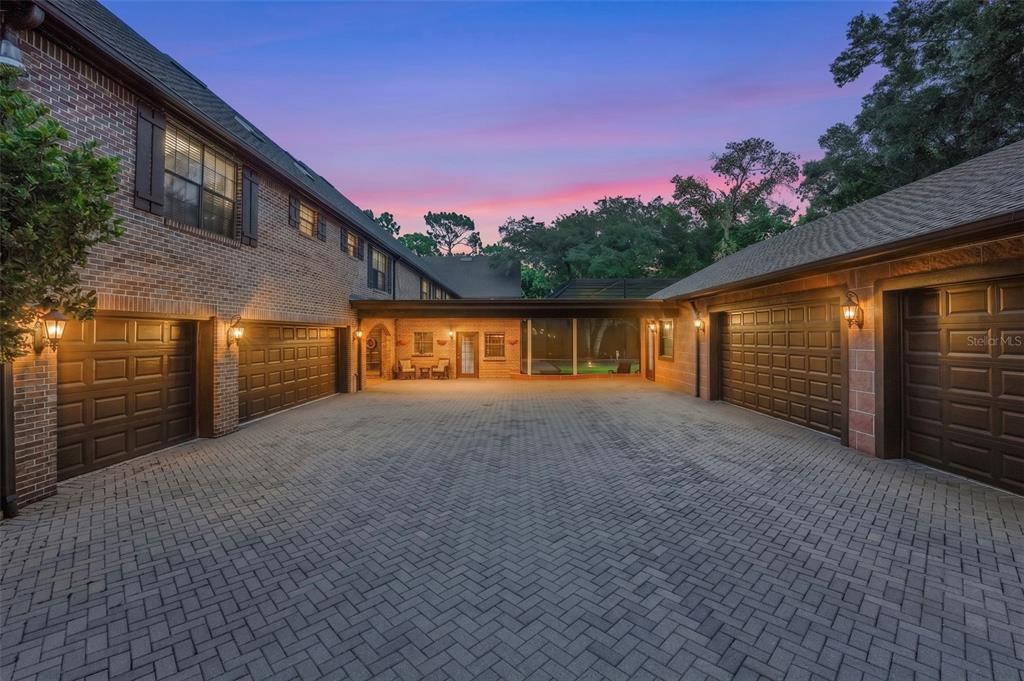 A brick house exterior features a large paved courtyard, multiple garage doors, and a covered walkway — 810 SWEETWATER CLUB BOULEVARD, LONGWOOD, FL