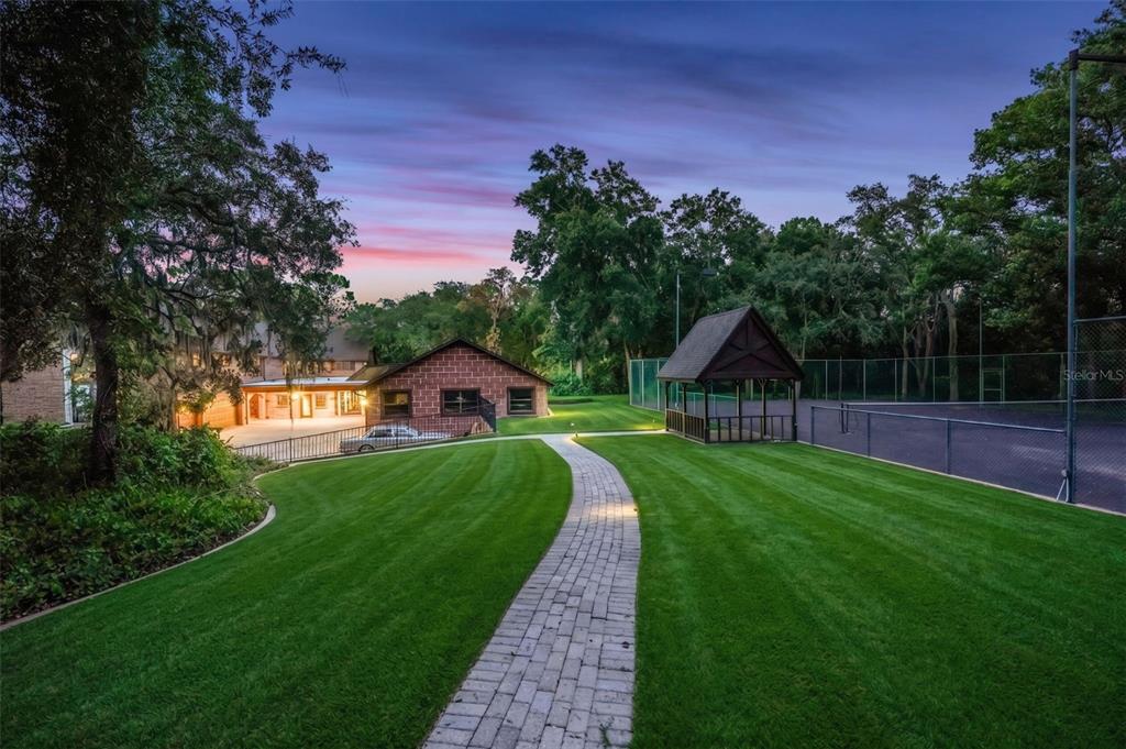 A brick building, a gazebo, and a tennis court sit on a lawn with a path — 810 SWEETWATER CLUB BOULEVARD, LONGWOOD, FL