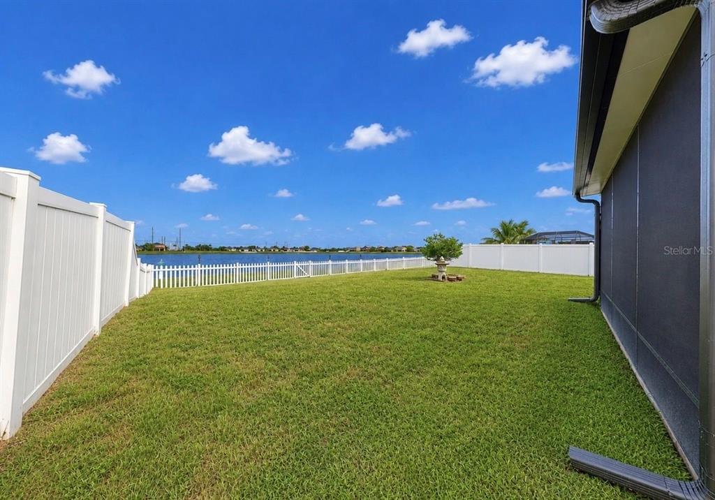 A grassy backyard features a white vinyl fence, a small decorative tree, and a lake view — 619 WABASH BREEZE CIRCLE, RUSKIN, FL