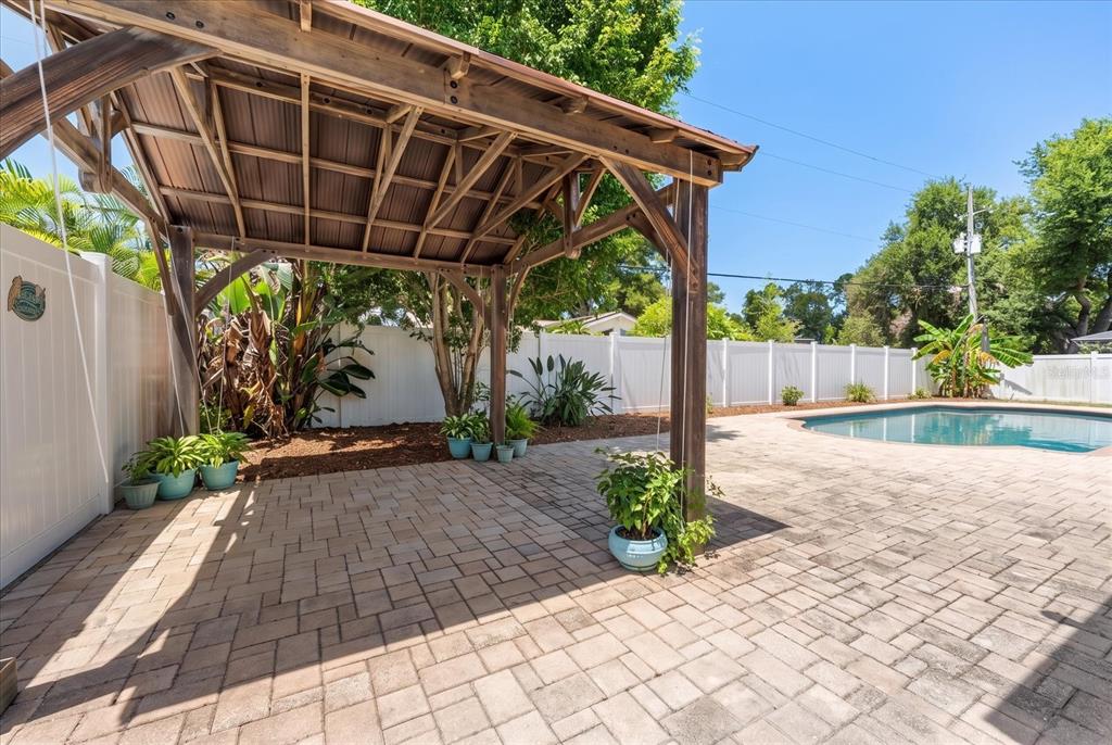 A wooden gazebo stands on a paved patio next to a swimming pool and fence — 10928 118TH STREET, SEMINOLE, FL