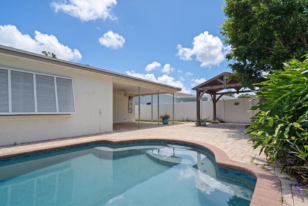 A backyard features a swimming pool, a paved patio, a covered porch, and a wooden pergola — 10928 118TH STREET, SEMINOLE, FL