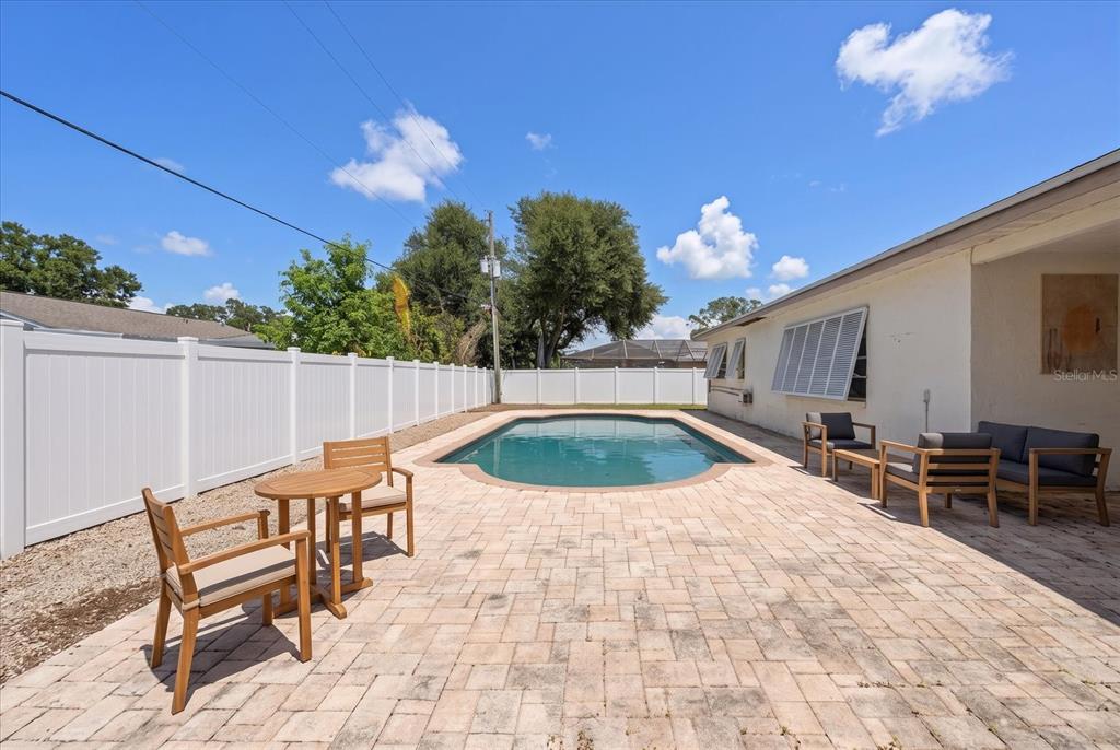 A backyard patio features a swimming pool, outdoor furniture, and a white vinyl privacy fence — 10928 118TH STREET, SEMINOLE, FL