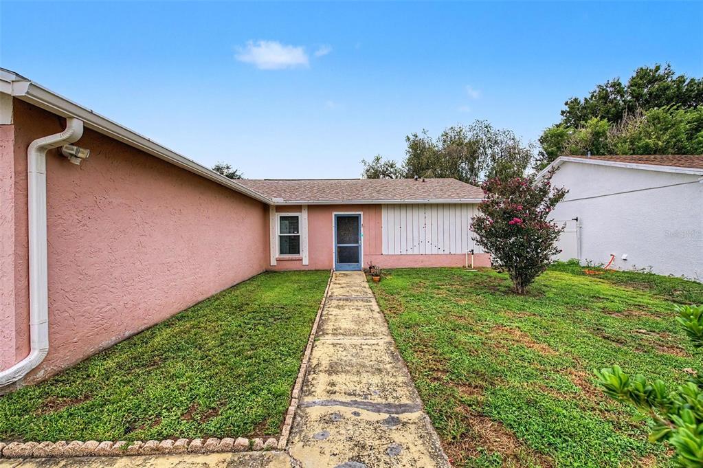 A pink stucco house exterior features a concrete walkway leading to a central front door — 1004 COOLWOOD PLACE, BRANDON, FL