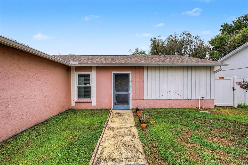 The exterior of a single-story house features pink stucco walls, white vertical siding, and a walkway — 1004 COOLWOOD PLACE, BRANDON, FL