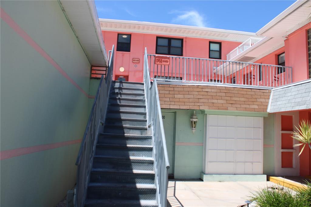 An exterior view of a pink and green building with metal stairs leading to a balcony — 6800 SUNSET WAY UNIT 1708, ST PETE BEACH, FL