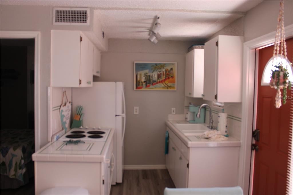 A small kitchen features white cabinets, tiled countertops, a white refrigerator, and a red door — 6800 SUNSET WAY UNIT 1708, ST PETE BEACH, FL
