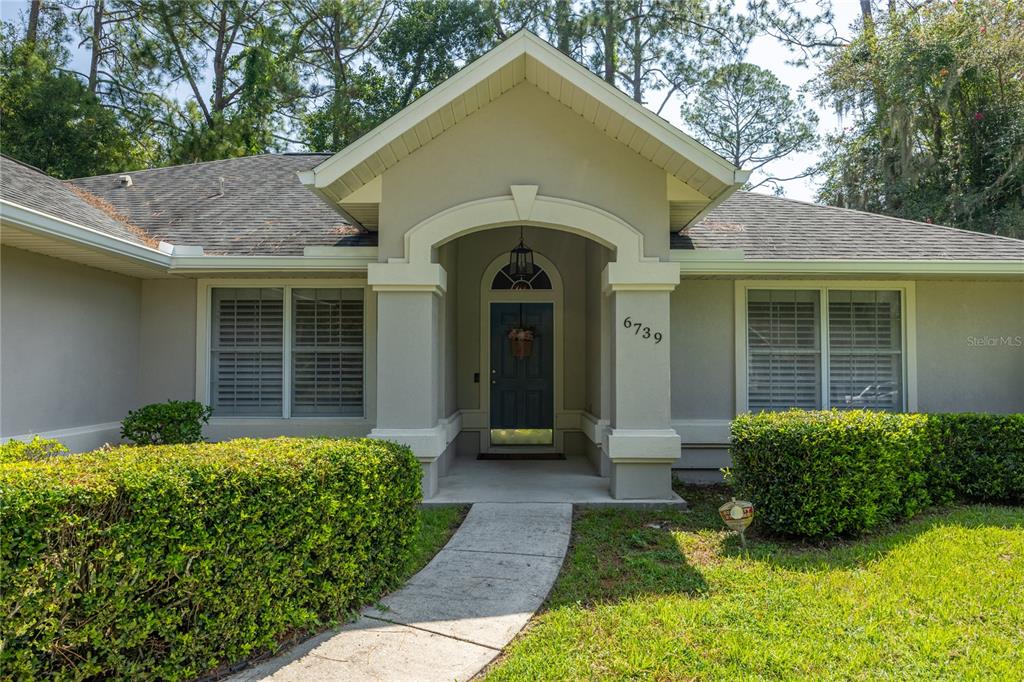 A front exterior view of a house with a covered entryway and manicured hedges — 6739 NW 34TH TERRACE, GAINESVILLE, FL