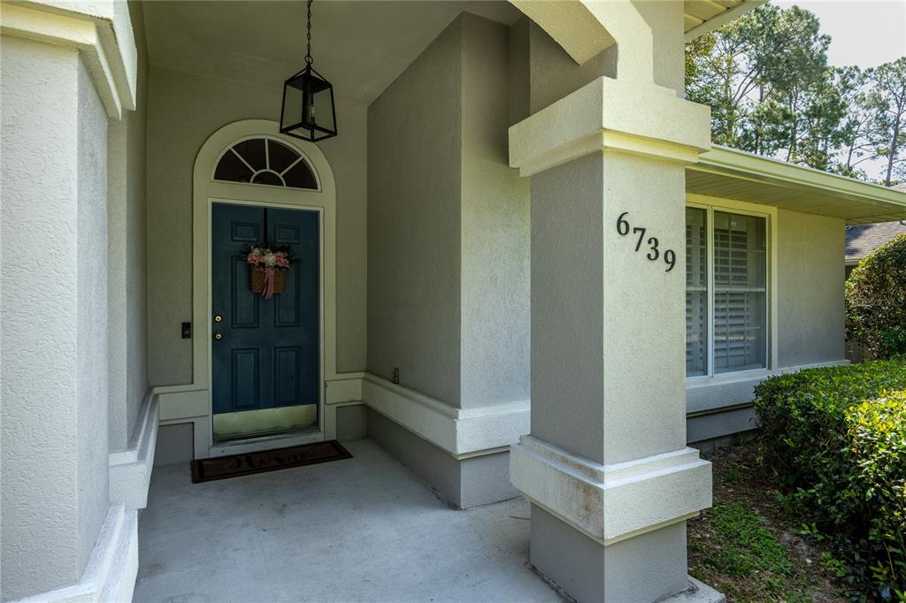 A covered front porch features a blue door, a hanging lantern, and house numbers — 6739 NW 34TH TERRACE, GAINESVILLE, FL