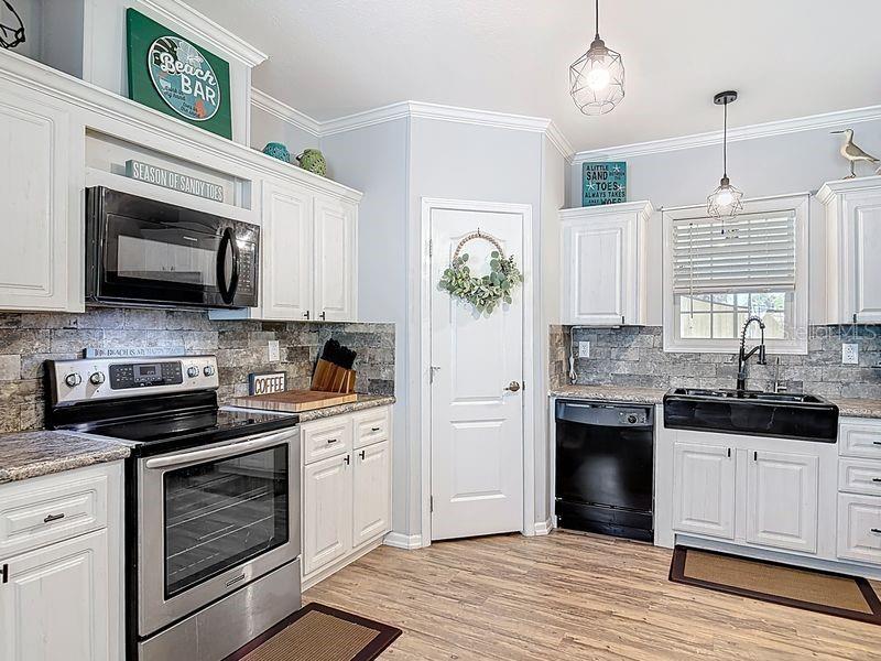 A kitchen features white cabinets, stainless steel appliances, a black farmhouse sink, and stone backsplash — 102 ASH STREET, EDGEWATER, FL