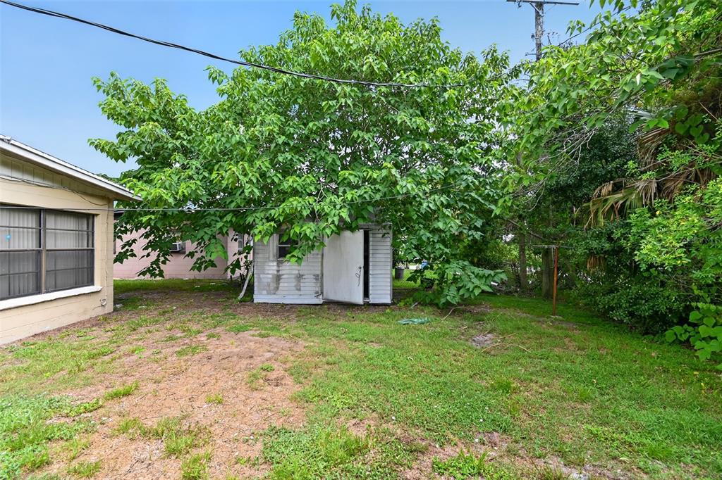 A small white shed sits in a grassy backyard beneath a large, leafy tree — 120 POLARIS STREET, COCOA, FL