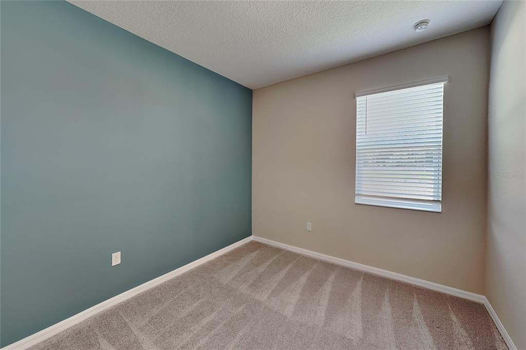 A bedroom features a teal accent wall, beige walls, carpeted flooring, and a window with blinds — 805 LEMON AVENUE, FRUITLAND PARK, FL