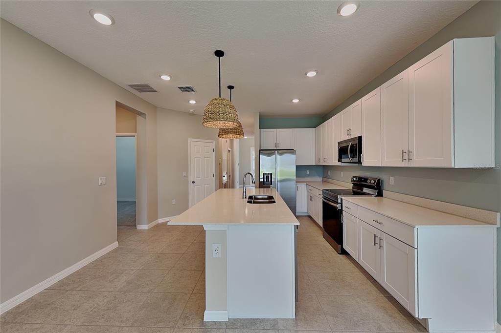 A kitchen features white cabinets, a central island with a sink, and stainless steel appliances — 805 LEMON AVENUE, FRUITLAND PARK, FL